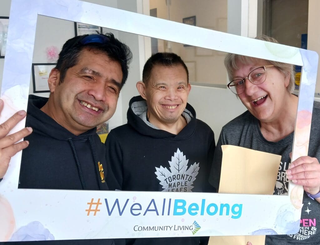 Three smiling people holding a ‘#WeAllBelong’ frame.