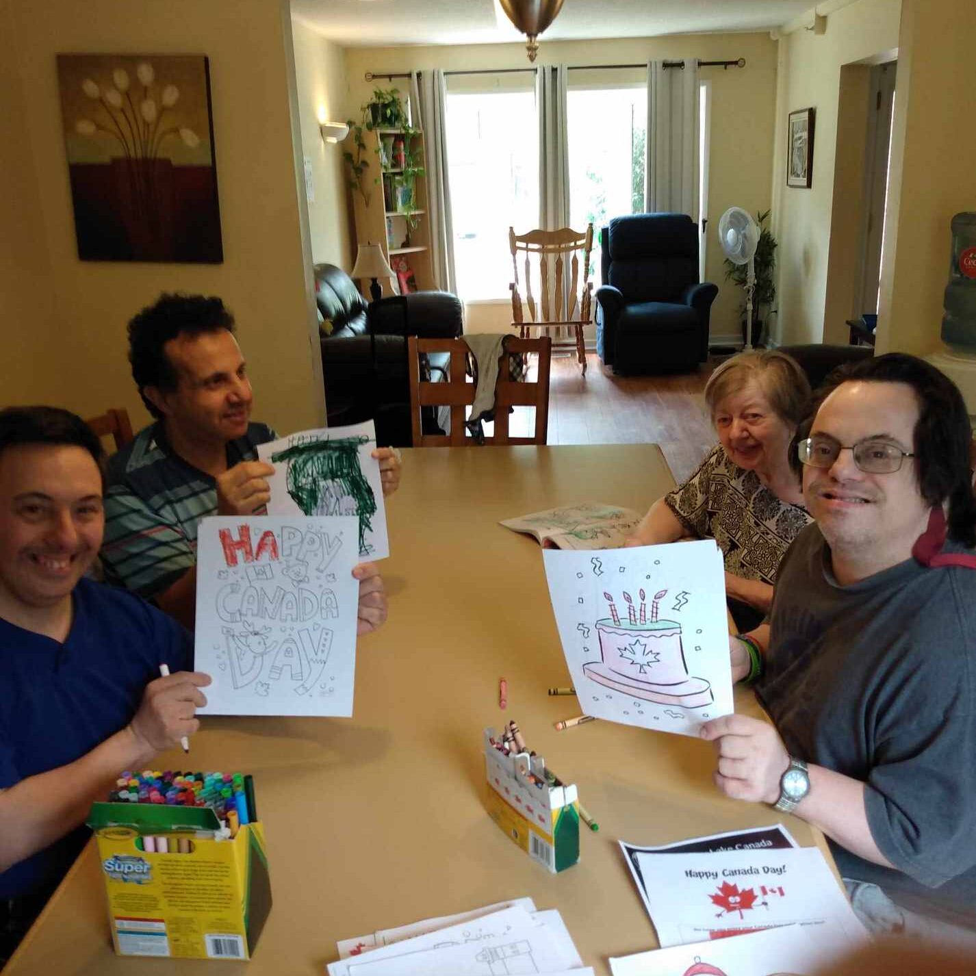 4 roomates, sitting a the dining table colouring and showing their art to the camera