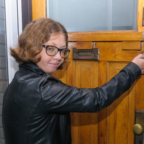 A woman at her front door, with keys in the lock about to open it