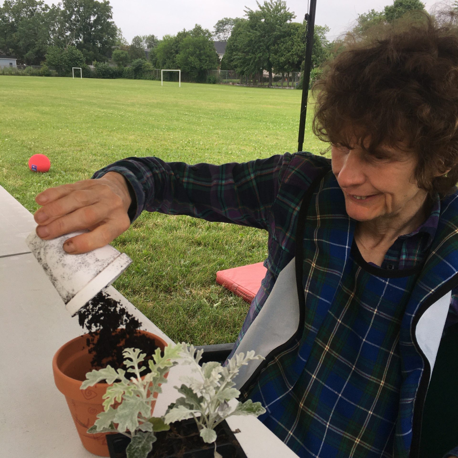 A resisent pouring soil into a pot, sitting outside at a table